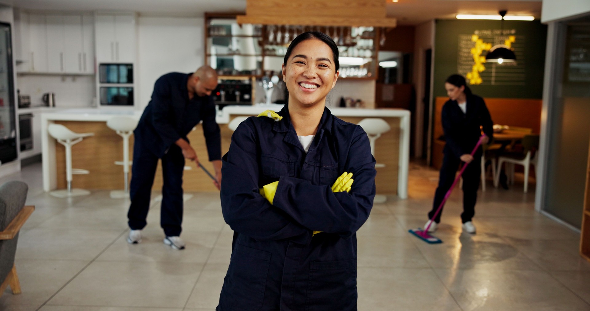 Woman, portrait and janitor with smile for maintenance job, hygiene and arms crossed with team in uniform. Pride, happy and cleaner with colleagues mop floors, overalls or confident at workplace