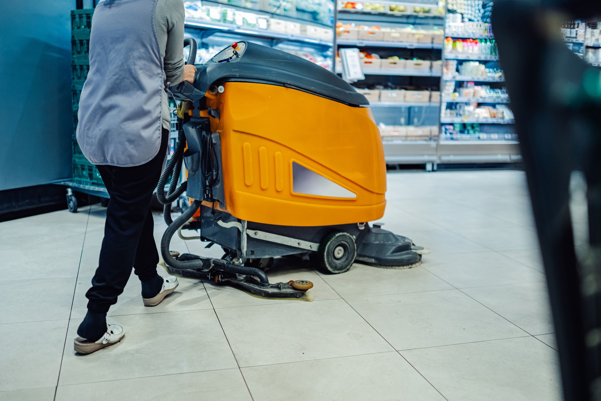 Cleaning lady using a floor scrubber machine in a supermarket