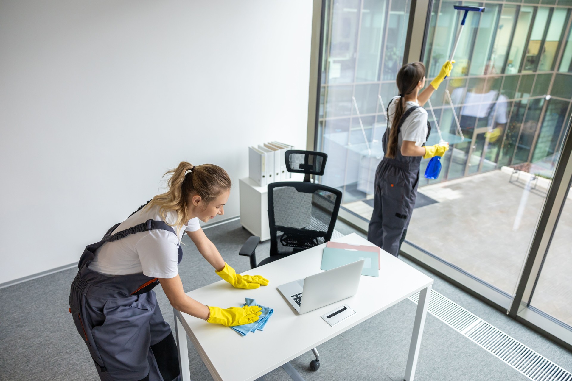 Blonde young woman in yellow gloves cleaning the table in the office