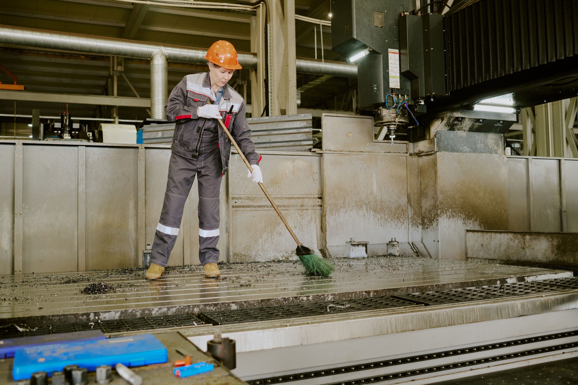 Middle Aged Caucasian Woman Cleaning Industrial Workshop Floor with Broom