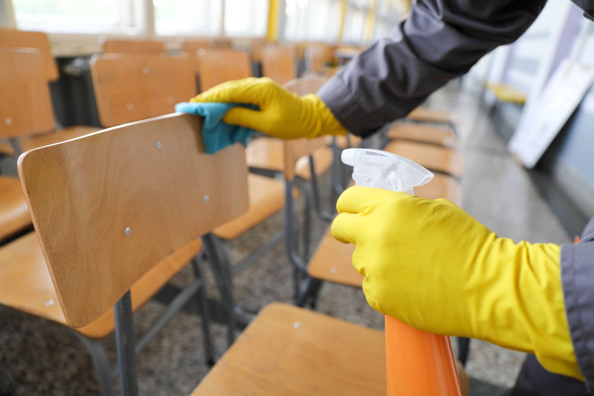 Senior Man Cleaning Chairs with Pump Sprayer and Cloth in School Classroom